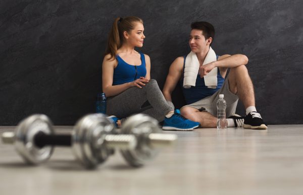 Focused fitness couple and two blurred dumbbells on floor at gym. Weight exercise, powerlifting, bodybuilding concept, copy space